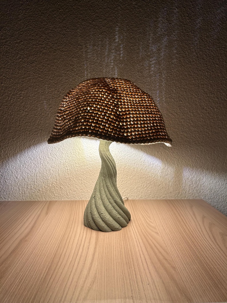Handmade mushroom lamp with a twisted sculptural base and handwoven brown shade. Emits a warm, cozy light that creates soft shadows on the wall, perfect for nightstands or ambient decor.