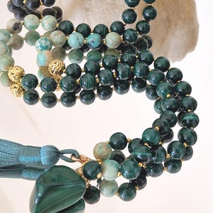 Peut inclure: Gros plan de plusieurs colliers de perles dans des tons de vert, de sarcelle et de noir. Les colliers comportent des perles rondes et des accents dorés. Un collier a un grand pendentif vert poli et un pompon sarcelle.