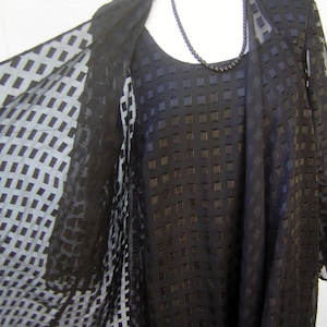 May include: A black sheer dress with a geometric pattern. The dress has a long sleeve and a scoop neck. The dress is layered over a black dress with a similar geometric pattern.