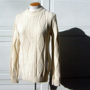 May include: A cream-colored cable knit sweater with a round neckline. The sweater is on a white mannequin.