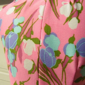 K&ouml;nnte beinhalten: Pinkfarbener Stoff mit einem Blumenmuster mit wei&szlig;en, blauen und gr&uuml;nen Bl&uuml;ten. Der Stoff hat eine glatte Textur.