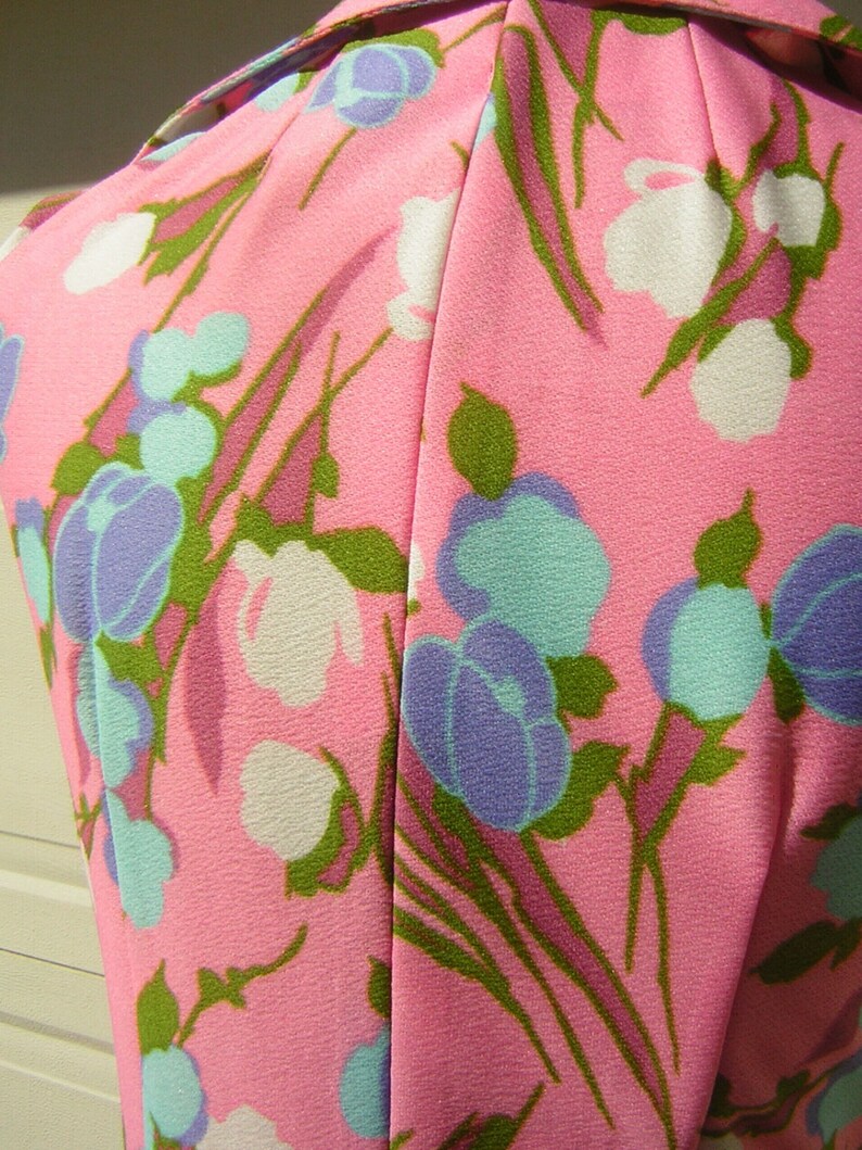K&ouml;nnte beinhalten: Pinkfarbener Stoff mit einem Blumenmuster mit wei&szlig;en, blauen und gr&uuml;nen Bl&uuml;ten. Der Stoff hat eine glatte Textur.