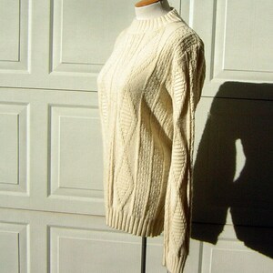 May include: A cream-colored cable knit sweater with a mock neck and long sleeves.