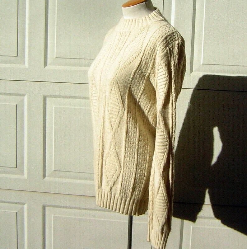 May include: A cream-colored cable knit sweater with a mock neck and long sleeves.
