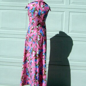 K&ouml;nnte beinhalten: Ein pinkfarbenes Maxikleid mit wei&szlig;em Kragen und einem Blumendruck mit blauen, wei&szlig;en und rosa Bl&uuml;ten. Das Kleid ist &auml;rmellos und hat einen taillierten Oberteil.