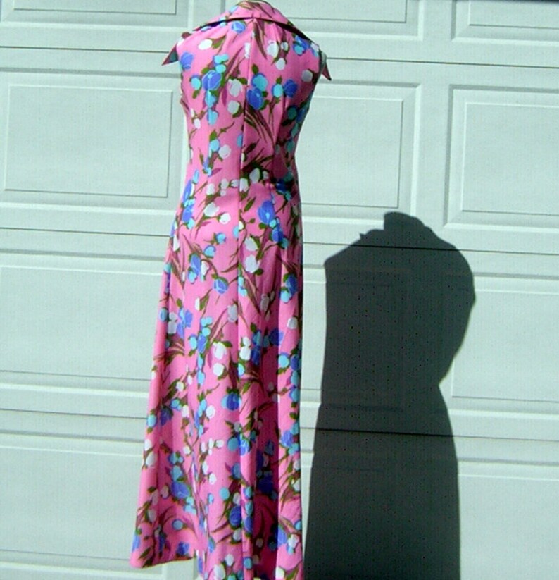 K&ouml;nnte beinhalten: Ein pinkfarbenes Maxikleid mit wei&szlig;em Kragen und einem Blumendruck mit blauen, wei&szlig;en und rosa Bl&uuml;ten. Das Kleid ist &auml;rmellos und hat einen taillierten Oberteil.