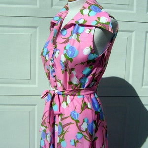 K&ouml;nnte beinhalten: Ein pinkfarbenes, &auml;rmelloses Kleid mit einem wei&szlig;en und blauen Blumendruck. Das Kleid hat einen gro&szlig;en Kragen und einen Bindeg&uuml;rtel.