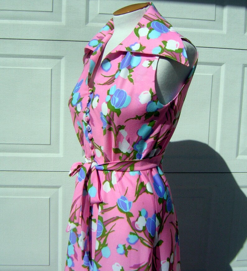 K&ouml;nnte beinhalten: Ein pinkfarbenes, &auml;rmelloses Kleid mit einem wei&szlig;en und blauen Blumendruck. Das Kleid hat einen gro&szlig;en Kragen und einen Bindeg&uuml;rtel.
