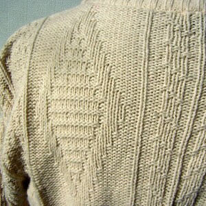 May include: A close-up of a cream-colored knitted sweater with a textured pattern. The sweater is made of a soft, comfortable material.
