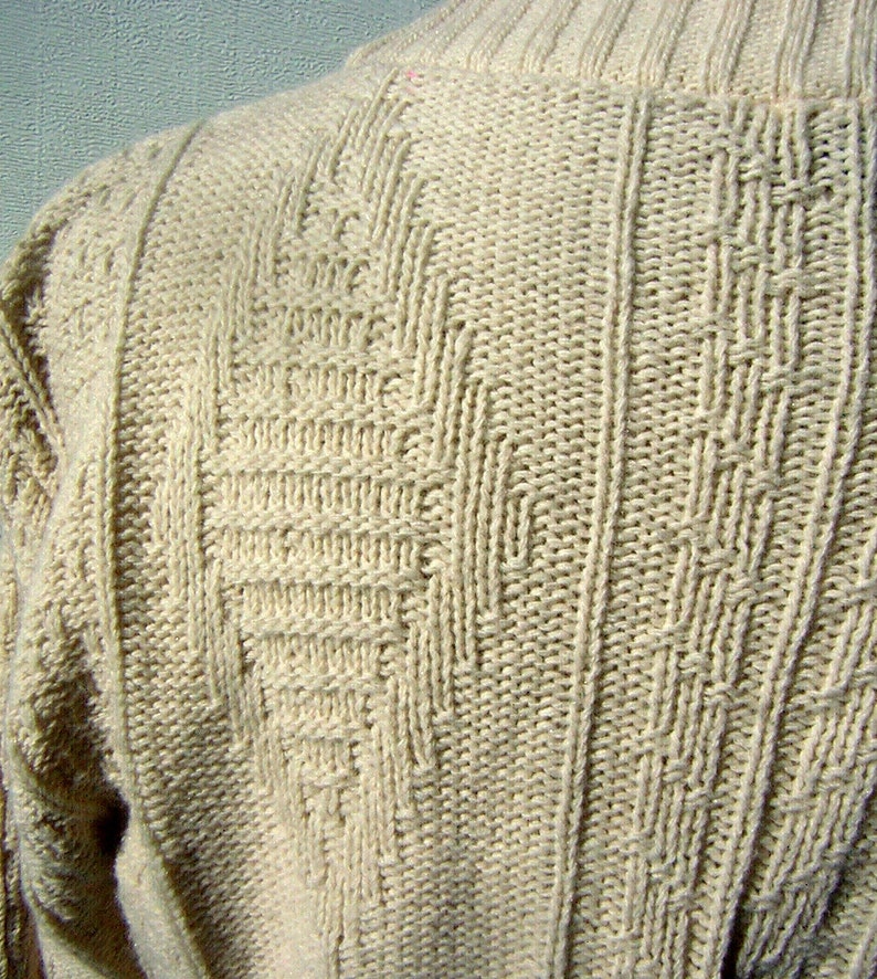 May include: A close-up of a cream-colored knitted sweater with a textured pattern. The sweater is made of a soft, comfortable material.