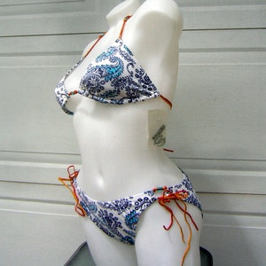 Könnte beinhalten: Weißer Bikini-Oberteil und -Unterteil mit einem blauen und weißen Paisley-Muster. Das Bikini-Oberteil hat verstellbare Träger und das Unterteil hat Bindebänder an den Seiten.