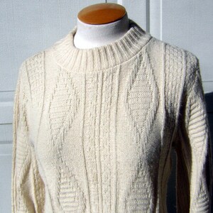 May include: A cream colored knitted sweater with a cable knit pattern.
