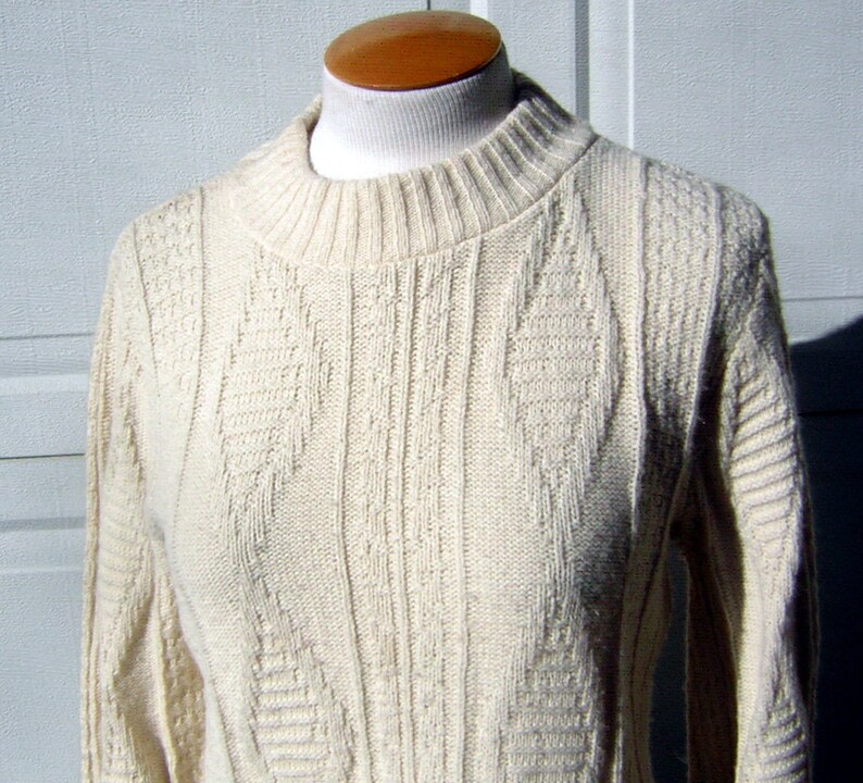 May include: A cream colored knitted sweater with a cable knit pattern.
