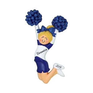 May include: A blue and white cheerleader ornament with blonde hair and a blue pom-pom in each hand. The ornament is personalized with the name "Veronica" and the year "2019".