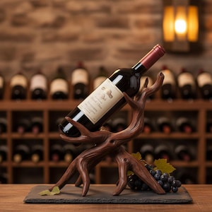Puede incluir: Un soporte decorativo de madera para botellas de vino con diseño de rama de árbol. Sostiene una botella de vino tinto, con un racimo de uvas y hojas sobre una base de pizarra. La botella de vino tiene una etiqueta blanca.
