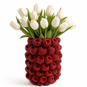 Puede incluir: Un jarrón rojo con una superficie texturizada, lleno de tulipanes blancos. El jarrón tiene un diseño único, que se asemeja a un racimo de frambuesas. Los tulipanes tienen tallos y hojas verdes, creando un contraste llamativo con el jarrón rojo.