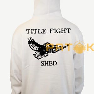 May include: White hooded sweatshirt featuring a black owl graphic and the text "TITLE FIGHT SHED". The design is printed on the back of the garment. The hoodie has a hood and long sleeves.