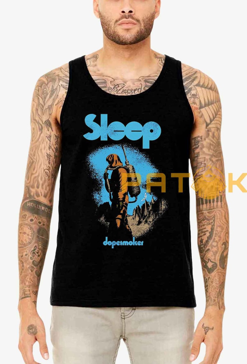 Pu&ograve; includere: Canotta nera con il nome della band "Sleep" in blu, sopra un'illustrazione di una figura con uno zaino in un paesaggio arancione e blu. La parola "dopesmoker" &egrave; stampata sotto.