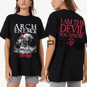 以下が含まれることがあります： 黒いTシャツ。前面にはバンド名「ARCH ENEMY」とクリーチャーのグラフィック、そして「Paper Tiger」の文字。背面には「I AM THE DEVIL YOU KNOW」の文字と五芒星のシンボルが赤色でプリントされています。