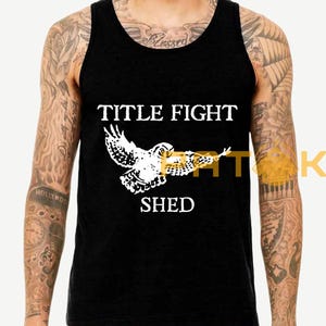May include: Black vest top featuring the text "TITLE FIGHT SHED" in white, and a white graphic of an owl. The top is sleeveless with a rounded neckline. The owl graphic has outstretched wings.