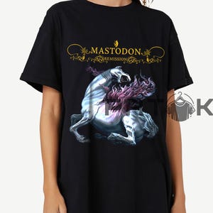 May include: Black t-shirt featuring the band name "Mastodon" in gold script above a graphic of a rearing, mythical creature with a flowing mane. The word "Remission" is below the band name.