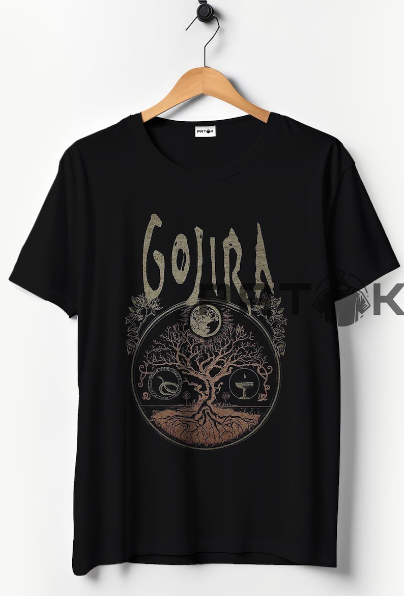 May include: Black t-shirt featuring the band name "GOJIRA" in a stylized font above a circular graphic. The graphic includes a tree of life design with a moon and other symbols. The shirt is hanging on a wooden hanger.