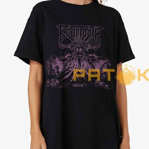 Puede incluir: Camiseta negra con el nombre de la banda "Beartooth" en morado, sobre un gráfico de una figura coronada y la palabra "BELOW". El diseño tiene un tema gótico.