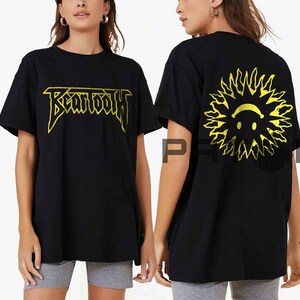 May include: Black t-shirt with the word "BEARTOOTH" in yellow, stylized lettering on the front. The back of the shirt features a yellow sun design with a smiling face. The shirt is a casual, oversized fit.