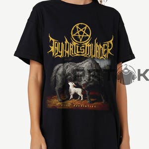 Puede incluir: Camiseta negra con el nombre de la banda 'Thy Art Is Murder' en letras doradas sobre un gráfico de dos lobos y un cordero. Las palabras 'Dear Desolation' están impresas debajo.