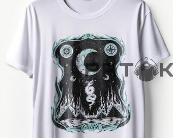 May include: White t-shirt featuring a black and teal graphic design. The design includes a crescent moon, stars, a snake, pyramids, and the word "GOJIRA". The shirt is hanging on a wooden hanger.
