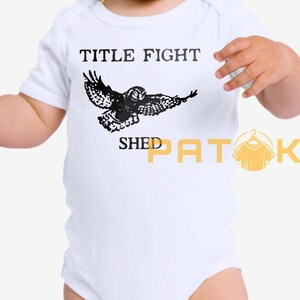 May include: White baby bodysuit featuring the text "TITLE FIGHT" and a black owl illustration. The words "SHED PATOK" are printed below the owl. The bodysuit has short sleeves.