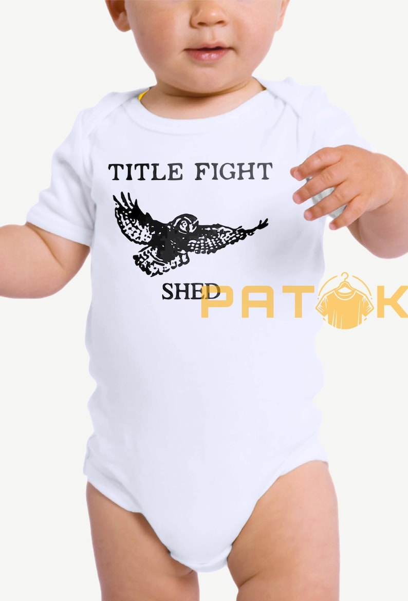May include: White baby bodysuit featuring the text "TITLE FIGHT" and a black owl illustration. The words "SHED PATOK" are printed below the owl. The bodysuit has short sleeves.