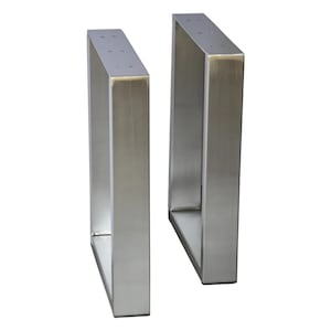 May include: Two rectangular table legs made of brushed stainless steel. Each leg features a flat, vertical frame with a hollow center and a top mounting plate with pre-drilled holes for attachment to a tabletop surface.