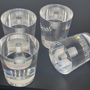 May include: Four clear acrylic furniture legs with a cylindrical design. Each leg features a threaded metal insert for secure attachment. The legs are transparent, allowing light to pass through, and are suitable for various furniture types.