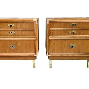 May include: Two matching wooden nightstands with three drawers each. The nightstands have brass hardware and corner accents. The legs are also brass. The wood has a warm, medium tone.