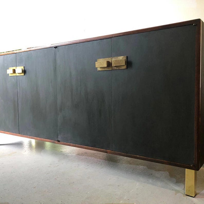 May include: A long, dark gray cabinet with a rectangular shape. The cabinet has a dark wood frame and gold-colored handles and legs. The cabinet doors are a solid, matte gray color.