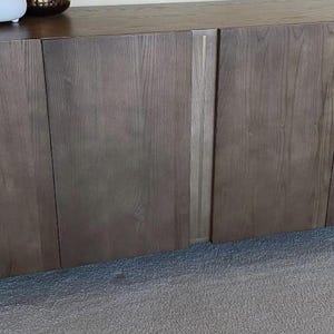 May include: A modern, dark wood cabinet with four doors and brushed metal legs. The cabinet has a natural wood grain finish and a rectangular shape. Decorative items sit on top.
