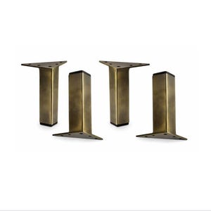 May include: Four antique brass-colored furniture legs. Each leg has a triangular top, a rectangular body, and a black square base. The legs are designed for furniture and have a vintage aesthetic.