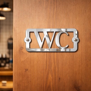 May include: A shiny, silver WC sign is mounted on a wooden door. The sign is rectangular with rounded corners and is attached with small, silver rivets. The letters WC are cut out of the metal. The door has a natural wood grain.