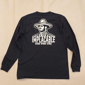 May include: Black long-sleeve shirt with a white graphic on the back. The graphic features a stylized image of a man in a hat and the word "IMPLACABLE" above "HARD WORK ETHIC". The shirt has a crew neck and long sleeves.