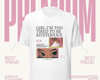May include: A white t-shirt featuring the black text GIRL I'M TOO TIRED TO BE MYSTERIOUS. Below the text are two rectangular graphic panels showing a stylized illustration of a person with pink hair and sunglasses, along with the text WAITING TO BE PERFECT KILLS MOMENTUM. STARTING GETS YOU MOVING.