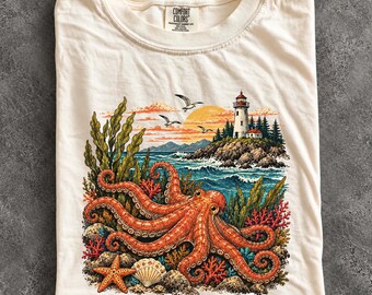 May include: An ivory t-shirt featuring a graphic print of a large orange octopus surrounded by coral, seaweed, and a starfish. The background shows a coastal scene with a lighthouse on a rocky cliff, a sunset, and seagulls flying over the ocean.