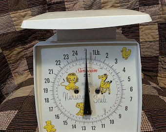 May include: A vintage white Sunbeam Nursery Scale with a weight capacity of 11.3 kg. The scale face features cartoon animal illustrations and a black needle. The scale has a white top and a square base.