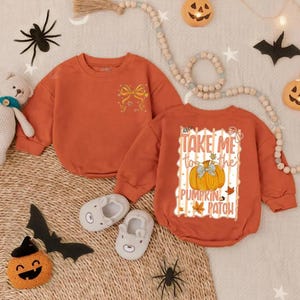May include: Two orange baby rompers with long sleeves. One has a bow design, the other says "Take Me to the Pumpkin Patch" with a pumpkin graphic. The image includes Halloween decorations like spiders and pumpkins.
