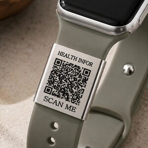 May include: A smartwatch with an olive green silicone band featuring a rectangular silver metal charm engraved with a QR code, the text HEALTH INFOR, and the text SCAN ME. The watch has a black screen and a silver side button with a red accent.