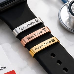 May include: A black smartwatch band featuring three metallic medical alert sliders in silver, rose gold, and gold. The sliders are engraved with the text Type 1 Diabetes, Blood Thinner, and Emergency Contact, each accompanied by a medical symbol.