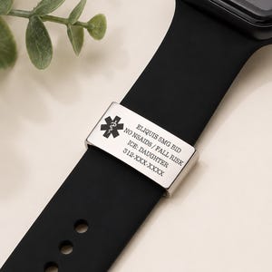 May include: A black smartwatch with a silicone band featuring a silver-toned metal medical alert tag. The tag displays a Star of Life symbol and engraved text: ELIQUIS 5MG BID, NO NSAIDS / FALL RISK, ICE: DAUGHTER, and 312-XXX-XXXX.