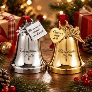 May include: Two metal Christmas bells, one silver and one gold, each engraved with "Christmas 2026". The silver bell features a snowflake charm and a square tag reading "The sweetest sounds are shared". The gold bell has a heart tag reading "Custom any text" and a "2026" charm with wings.