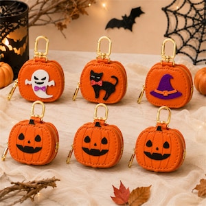 May include: Six orange pumpkin-shaped coin pouches with gold-tone metal lobster clasps. Three pouches feature felt appliqués: a white ghost with a purple bow, a black cat with a red bow, and a purple witch hat. Three pouches feature jack-o'-lantern faces.
