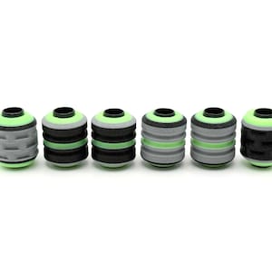 May include: A set of six cylindrical beads arranged in a horizontal row. Each bead features a central black or grey textured core with horizontal grooves, accented by bright neon green rings at the top and bottom edges and a black circular opening.